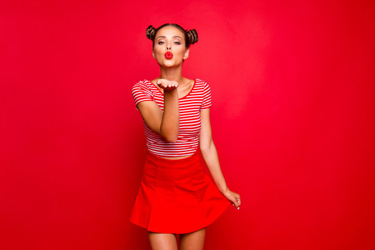Cute girl send a kiss for you! Adorable young girl with nice make up wearing striped tshirt and red skirt isolated on bright background and sends air kiss from open palm