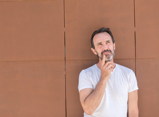 Handsome senior man standing over wall serious face thinking about question, very confused idea