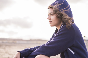 beautiful girl sitting at the beach outdoor in summer holiday.  lost in her thoughts with independence and freedom concept. bright sky with clouds in background. bad weather around the pretty woman