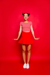 Full-length vertical portrait of happy young girl wear in red skirt and striped tshirt stand upright look at the camera isolated on red background