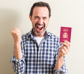 Senior man holding spanish passport screaming proud and celebrating victory and success very excited, cheering emotion