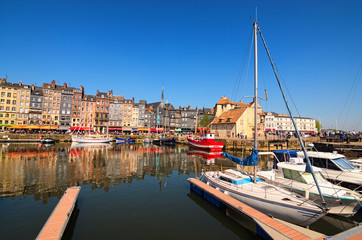 Fototapeta na wymiar HONFLEUR, FRANCE-MAY 05, 2018: Yachts in the Honfleur harbor in a spring day. Color houses and their reflection in water. Ancient The Lieutenancy Building (Fr: La Lieutenance) at the background