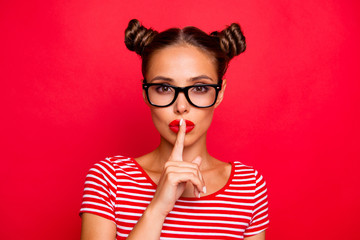 Shh! Portrait of attractive mysterious girl in glasses gesturing silence sign with forefinger red pout lips looking at camera isolated on red background - obrazy, fototapety, plakaty
