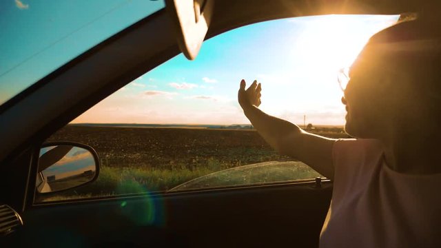 Teen Waves Her Hand In The Wind In car slow motion video. Young happy young girl drives a car a holds her hand out from the window. Road trip, lifestyle travel and freedom concept