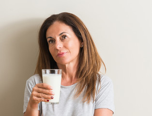 Middle age woman drinking a glass of fresh milk serious face thinking about question, very confused idea