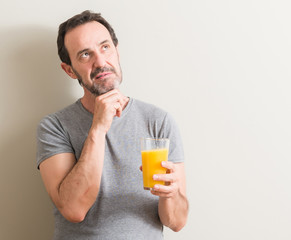 Fototapeta premium Senior man drinking orange juice in a glass serious face thinking about question, very confused idea