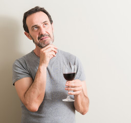 Senior man drinking red wine in a glass serious face thinking about question, very confused idea