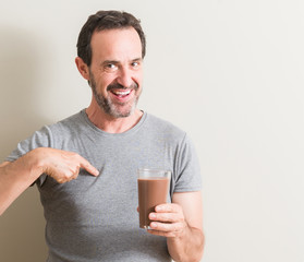 Senior man drinking chocolate milk shake with surprise face pointing finger to himself