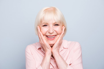 Old adult blonde glad excited cheerful astonished lady smiling, laughing, palms to cheeks, over grey background, isolated