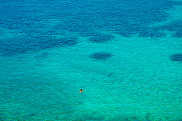 Fototapeta na wymiar A man is swimming into the endless crystal clear turquoise waters of Vaporia region in Syros greek island, Cyclades, Greece. 