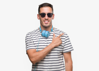 Handsome young man wearing headphones cheerful with a smile of face pointing with hand and finger up to the side with happy and natural expression on face looking at the camera.