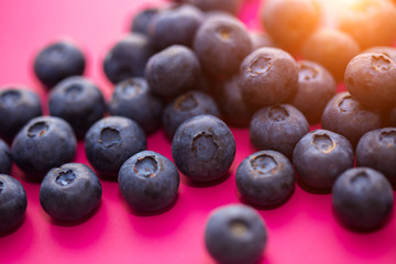 Close - up of ripe blueberries on a pink background in the sun, macro photo