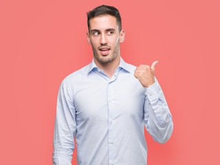 Handsome young businessman smiling with happy face looking and pointing to the side with thumb up.