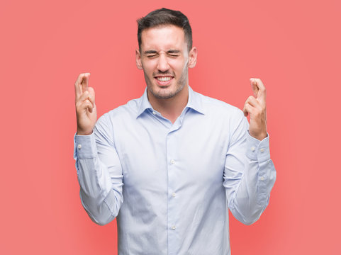 Handsome young businessman smiling crossing fingers with hope and eyes closed. Luck and superstitious concept. - Powered by Adobe