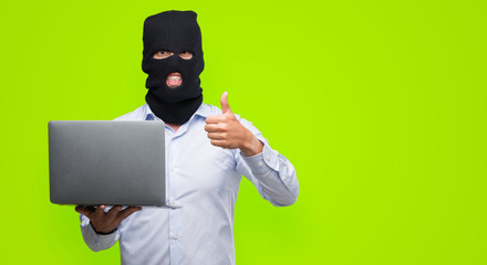 Business hacker man holding a computer laptop happy with big smile doing ok sign, thumb up with...