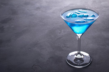 Blue cold cocktail in martini glass with ice and clear dew drops on  glass on a gray concrete background with space for text
