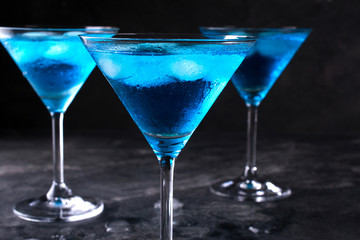 Three glasses of blue cold  martini cocktail with ice and clear dew drops on  glass on a gray concrete background , closeup shot