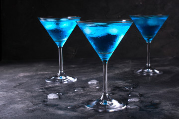 Blue cold cocktail in martini glass with ice and clear dew drops on  glass on a dark concrete background