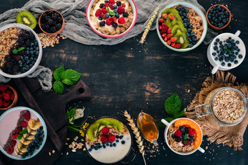 Oatmeal with yogurt, fruits and berries in plates. Breakfast. On a black wooden background. Top view. Free space for text.