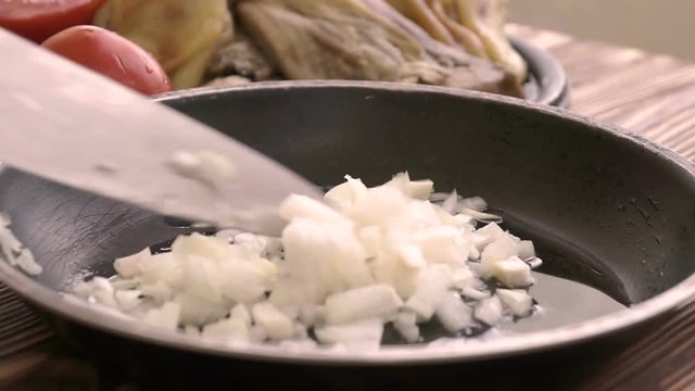 Chef puts chopped onion to the frying pan with hot sunflower oil.