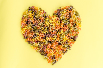 Heart shape made of colorful fusilli macaroni, on yellow background. Love pasta concept.