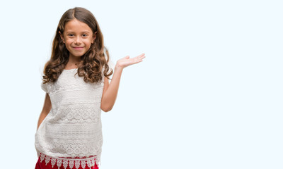 Brunette hispanic girl smiling cheerful presenting and pointing with palm of hand looking at the...