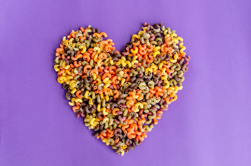 Heart shape made of colorful fusilli macaroni, on purple background. Love pasta concept.