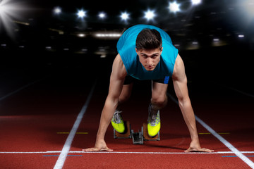 Sprinter leaving starting blocks on the running track in front of big modern stadium with lights....