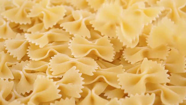 Food background, dried farfalle pasta falling on a heap, top view, slow motion