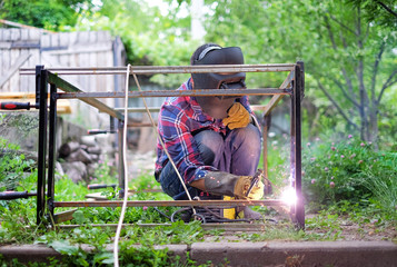 Man in a protective mask welding metal construction outside on a summer day