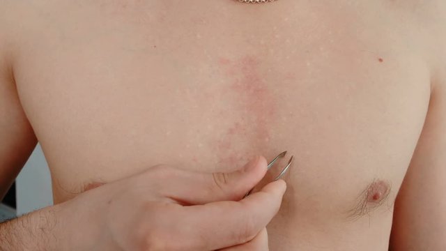 Close-up of a man's hand will pluck out his chest hair.