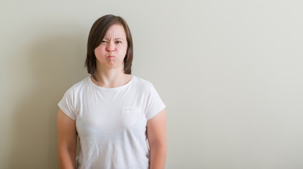 Obraz premium Down syndrome woman standing over wall puffing cheeks with funny face. Mouth inflated with air, crazy expression.