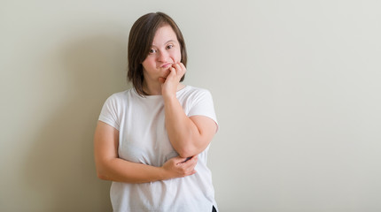 Down syndrome woman standing over wall looking stressed and nervous with hands on mouth biting nails. Anxiety problem.