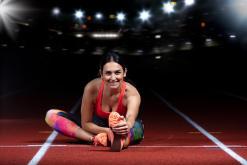young athletic woman doing exercises on flexibility. stretching legs sitting track stadium, night with reflectors - obrazy, fototapety, plakaty