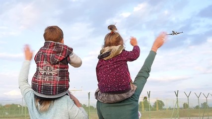 Two woman with a child on shoulders joyfully greeted a plane landing near airport wave hands