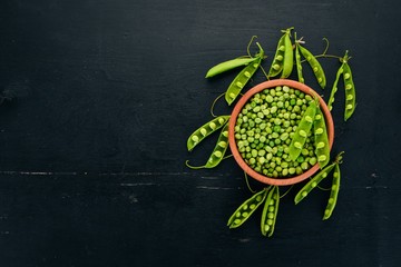 Green peas in a wooden plate. On a wooden background. Top view. Free space for your text.