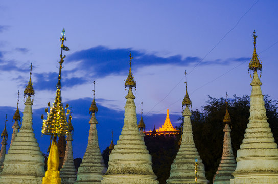 Top spires of the stupas in Sandar Mu Ni Paya, Mandalay, with illuminated shrine in the background