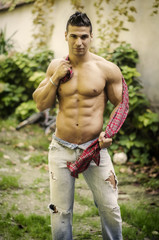 Handsome, athletic man playing with shirt, wearing jeans and showing muscular torso, abs, pecs and...