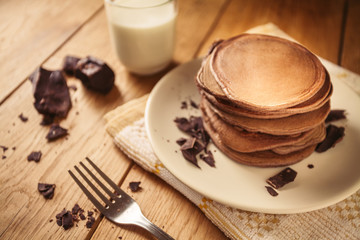 A view of delicious cocoa pancakes with dark chocolate and powdered sugar on a wooden table