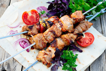 Barbecue. Juicy skewers of pork on pita bread. Decorated with herbs, tomatoes, pickled onion and basil, there is a red sauce next to it.