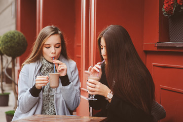 two happy girl friends talking and drinking coffee in autumn city in cafe. Meeting of good friends, young fashionable students with natural make up.
