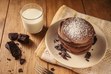 A view of delicious cocoa pancakes with dark chocolate and powdered sugar on a wooden table