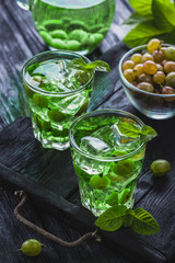 green gooseberry cocktail with ice and fresh mint on a black wooden table. refreshing summer drink