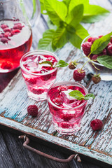Red raspberries cocktail with ice and fresh mint on a old wooden table. refreshing summer drink
