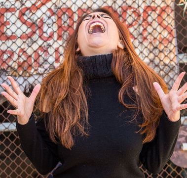 Mujer joven de pelo largo casta&ntilde;o gritando en la calle mientras agita los brazos y las manos