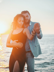 Portrait of young attractive couple dancing latin bachata near sea. Dance performed by a...