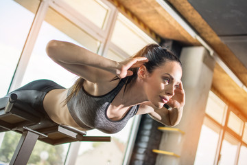 Beautiful young slim woman performing back-extension exercise on roman chair at gym.