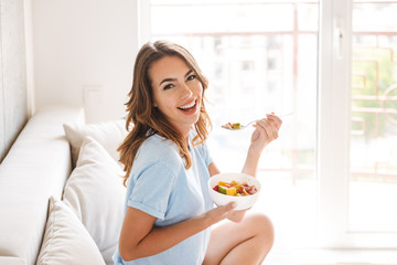 Cheerful young woman eating healthy breakfast - obrazy, fototapety, plakaty