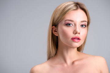 Naklejka premium beautiful young blonde woman looking at camera isolated on grey