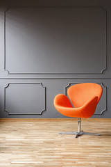 Modern orange armchair in minimal grey living room interior with wooden floor. Real photo